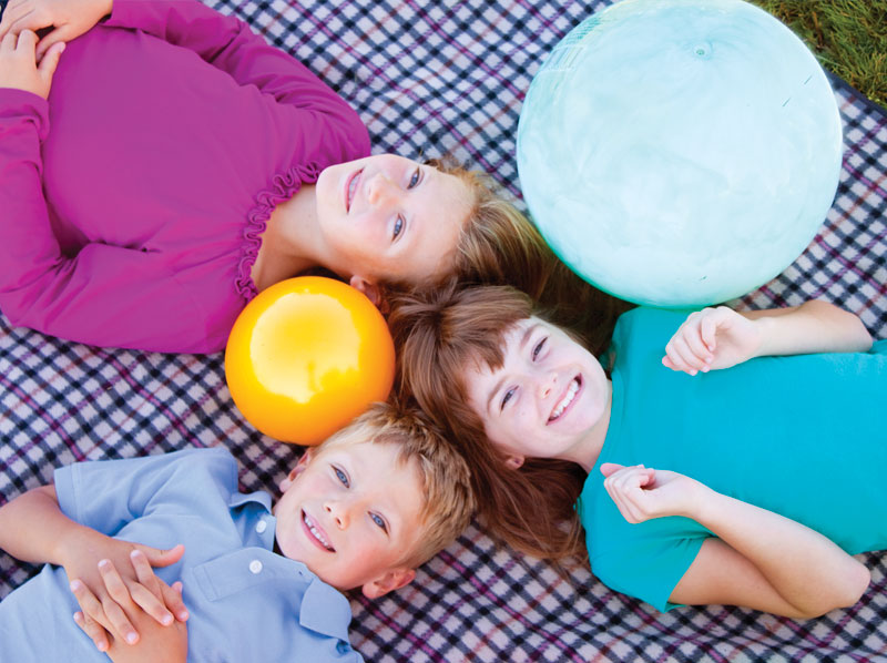 Two girls and a boy laying on a blanket with balls.